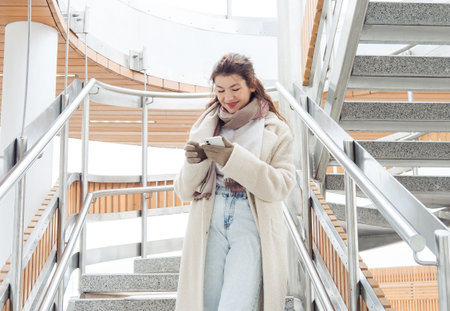 Woman in winter clothes talking on phone in the city. Young woman stay near modern stairs.の写真素材