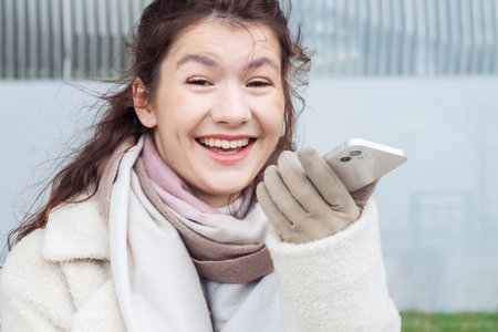 A young woman laughs and talks on speakerphone on a smartphone on a street in the city. Winter time.
