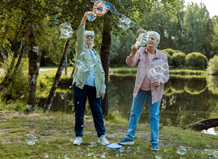 Lifestyle and people concept. Two elderly sisters blowing soap bubbles in a summer park. Happy twins.の写真素材