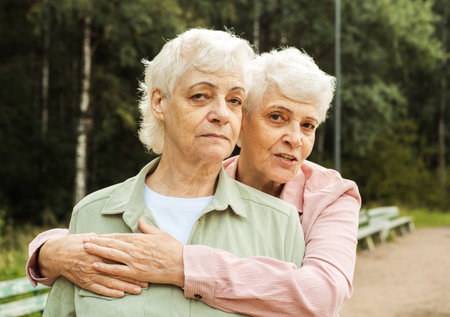 Two elderly sisters happily hugging and laughing on a summer day in the park. Lifestyle concept.