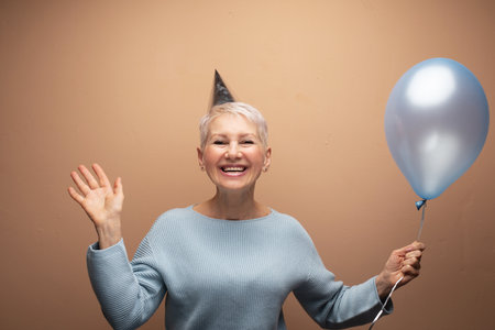 Beauitful happy elderly female wearing conical hat celebrating birthday.