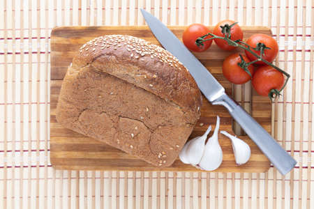 Fresh bread, garlic, tomatoes and a knife on a cutting board. Back of the reed. View from above
