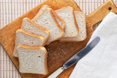 Fresh sliced bread nd a knife on a cutting board. Kitchen napkin. Back of the reed. View from above