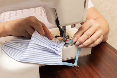 Woman hands using the sewing machine to sew the face medical mask. Homemade protective mask against virus.の写真素材