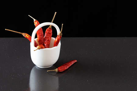 Dried red hot peppers in a white small clay basket. Dried pods of red chili peppers on a dark...
