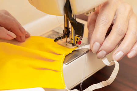 Woman hands using the sewing machine to sew the face medical mask. Homemade protective mask against...
