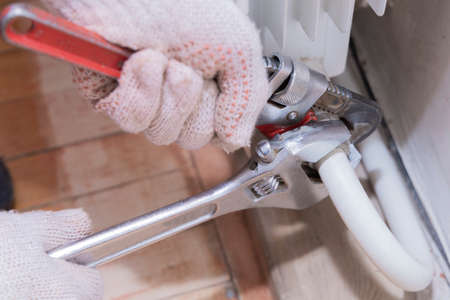 Hands of a man in gloves are installing the heater system in the house and checking pipes by the wrench. Tightening of leaking valve of heating pipe connections using pipe wrench. Closeup.の写真素材
