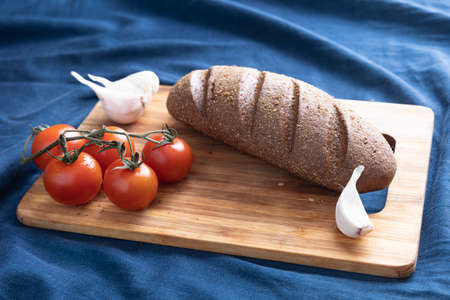 Fresh bread, tomato, garlic, knife on a cutting board. Dark blue background. Side view. Closeupの写真素材