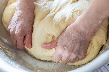 Kneading the dough in home. Hands of an elderly woman knead the dough in her home. 