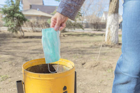 A woman throws a used  face masks into an urn. The virus season is over. Coronavirus is over