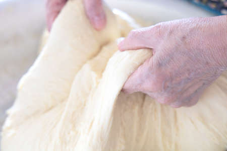 Kneading the dough in home. Hands of an elderly woman knead the dough in her home.