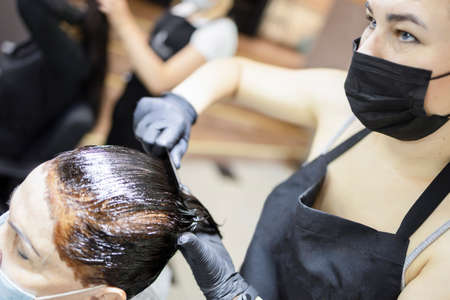 Hairdresser dyes woman hair. Hairdresser colorist dyes the hair of woman. Beautician, hand. Hairdressing during the coronavirusの写真素材