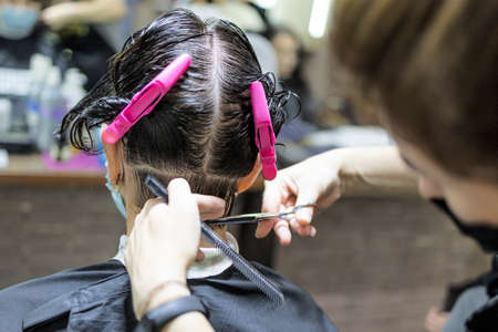 Hairdressing services during coronavirus. Hairdresser in face mask cuts hair of woman in face mask. Hairdressers cutting hair during COVID-19の写真素材