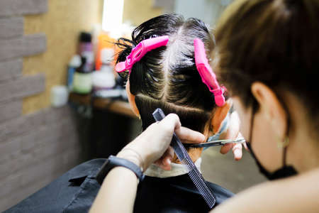 Hairdressing services during coronavirus. Hairdresser in face mask cuts hair of woman in face mask. Hairdressers cutting hair during COVID-19の写真素材