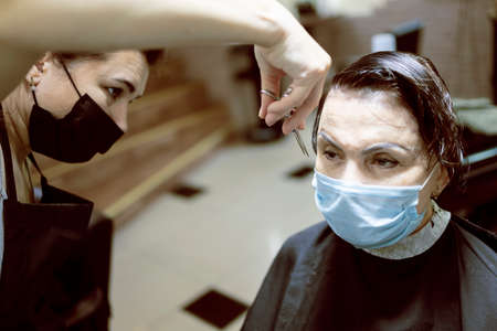 Hairdressing services during coronavirus. Hairdresser in face mask cuts hair of woman in face mask....