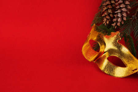 New Year. Gold mask. Green branches of pine tree. Red background. Cones. Blurred in some placesの写真素材