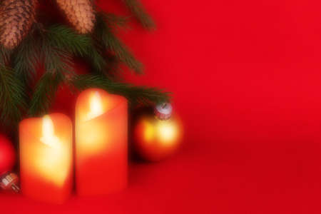 New Year. Christmas. Two artificial candles. Green branches of pine tree. Cones. Christmas balls. Red background. Blurred pictureの写真素材