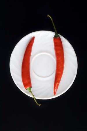 two chili peppers laying on the white plate with blcack backgroundの写真素材