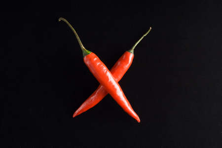 two red hot chili crossing peppers on the black velvet backgroundの写真素材