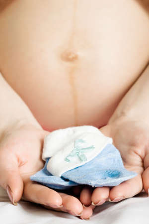 closeup pregnant woman holding blue socks in the hands