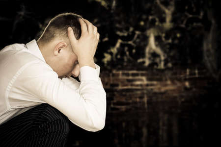 sad sitting young businessman with grunge wall background, copy space for the text