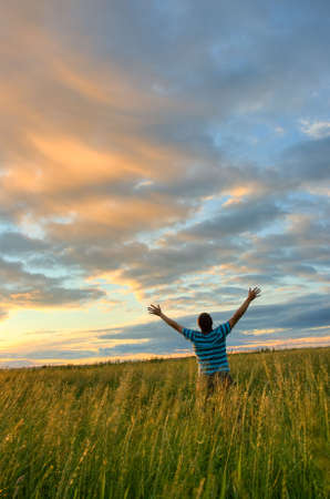young man rising hands over sunsetの写真素材
