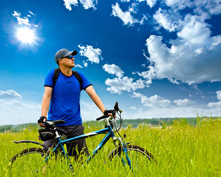 man with bike on green field under blue skies