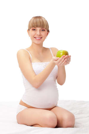 pregnant woman with green apple sitting on bed over whiteの写真素材