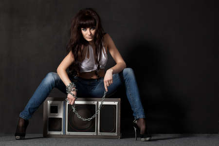 beautiful garage style weared woman sitting on speaker near black wallの写真素材