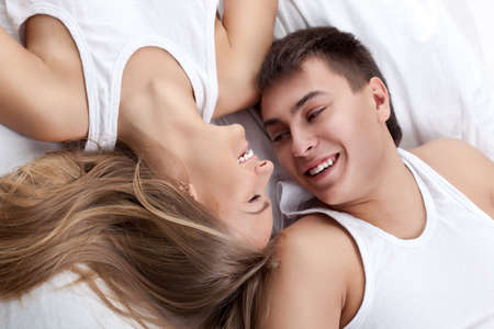 young adult couple lying on white bedの写真素材