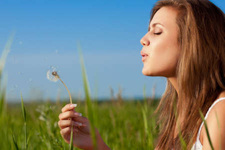 beautiful woman blowing to dandelio on green fieldの写真素材