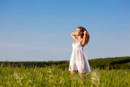 beautiful happy woman standing on green field over blue skiesの写真素材