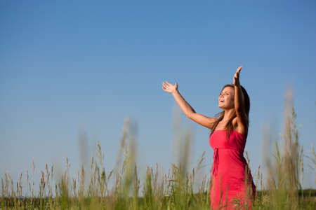 beautiful happy woman standing on green field over blue skiesの写真素材