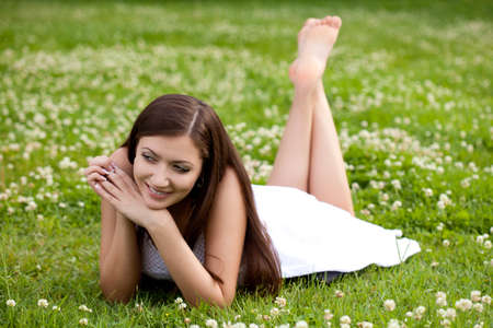 woman wearing white dress laying on grass in parkの写真素材