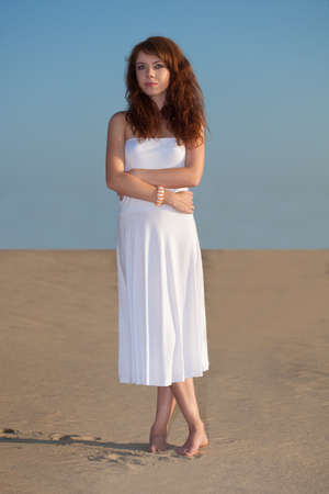red-haired beautiful woman walking on sand wearing white dressの写真素材