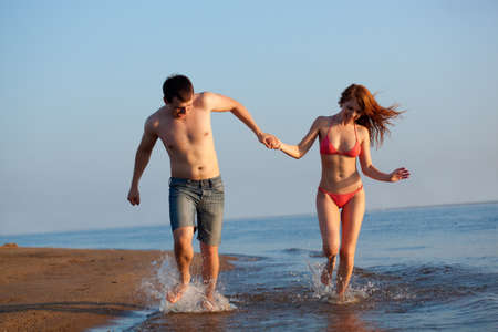 young adult happy couple running on beachの写真素材