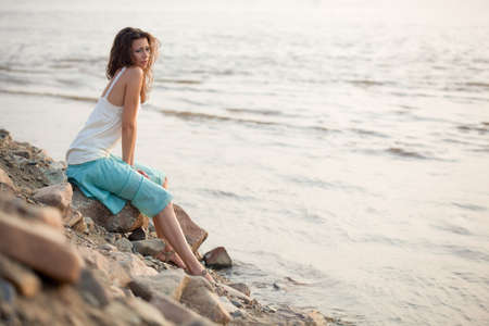 beautiful brunette  woman sitting on stone near waterの写真素材
