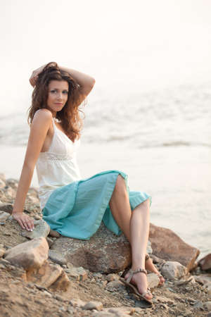 beautiful woman sitting on stone near water and holding hand on headの写真素材