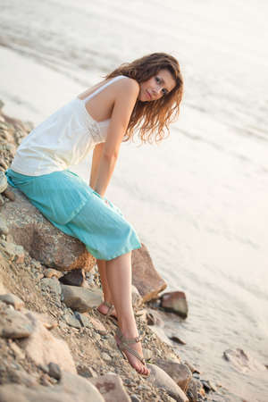 beautiful young woman sitting on stone near waterの写真素材