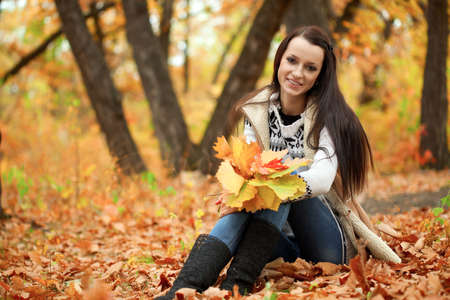 brunette woman sitting in autmn park and holding leavesの写真素材