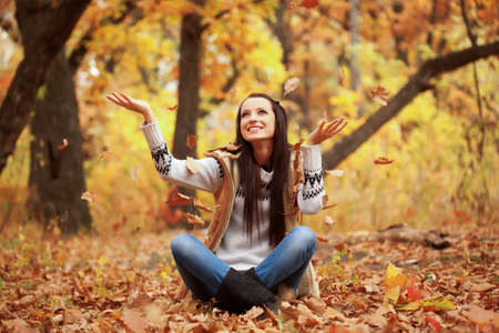 smiling woman sitting on fallen leaves in autmn park and rising up handsの写真素材