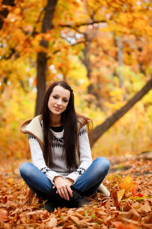 brunette woman sitting on fallen leaves in autmn parkの写真素材