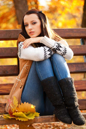 brunette woman sitting on brown bench and looking at cameraの写真素材