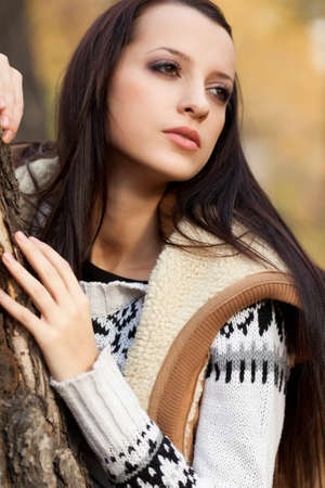 brunette woman standing near tree in autmn parkの写真素材