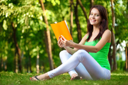 brunette woman reading book at green summer parkの写真素材