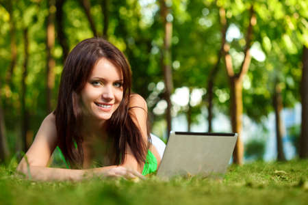 woman laying on grass with laptop in summer parkの写真素材