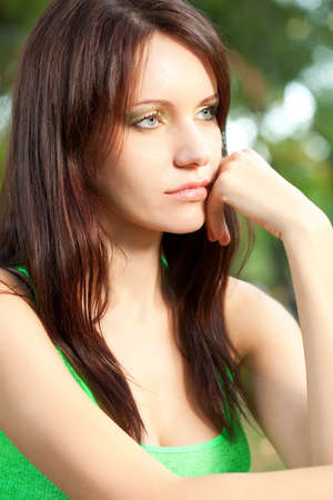 serious woman sitting under the tree at summer park closeup faceの写真素材