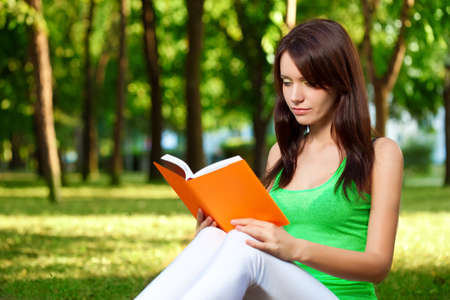 brunette beautiful woman reading book at summer parkの写真素材
