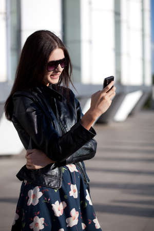 woman wearing sunglasses looking at phone outdoors portraitの写真素材