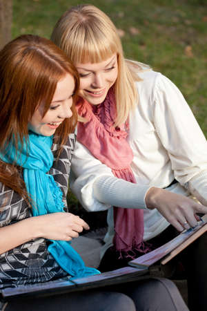 two laughing sisters with photo album in the summer parkの写真素材
